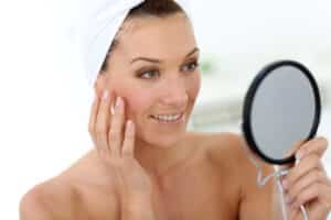 Mature woman admiring her beautiful skin in mirror after microneedling treatment.